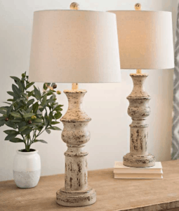 2 distressed cream skinny lamps with green plant sitting on table