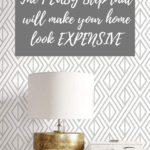 White and gray patterned wallpaper with white console table and lamp sitting on top on it with text overlay - The 1 easy step that will make your home look expensive.