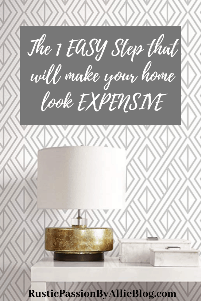 White and gray patterned wallpaper with white console table and lamp sitting on top on it with text overlay - The 1 easy step that will make your home look expensive.